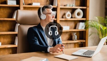 A man with headphones dressed in a suit sitting on a desk