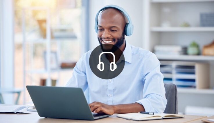 A man with white headphones smiling and looking at computer screen