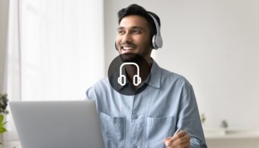 A man sitting in a desk with a computer and wearing headphones