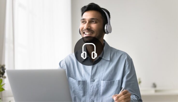 A man sitting in a desk with a computer and wearing headphones