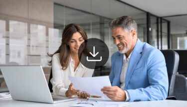 A man and a woman in an office setting looking at a document and smiling