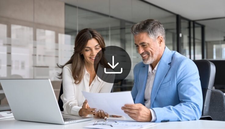 A man and a woman in an office setting looking at a document and smiling