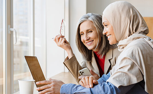 Two women smiling and looking into a computer screen