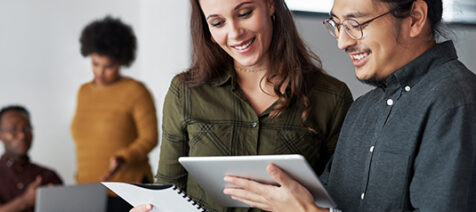 A man and a woman reviewing a document and looking at a tablet