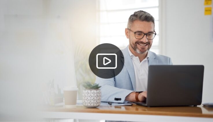 A man wearing a grey suit smiling and typing on his laptop computer