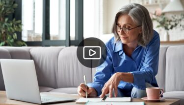 A woman with glasses writing on a paper while sitting in a couch