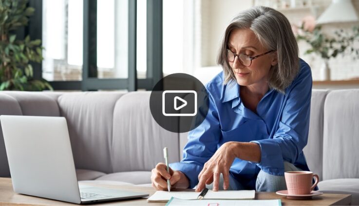 A woman with glasses writing on a paper while sitting in a couch