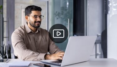 A man dressed in business casual sitting down and typing on laptop computer