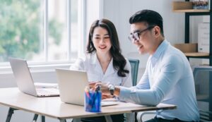 A woman and a man professionally dressed sitting down and looking at computer screens while smiling