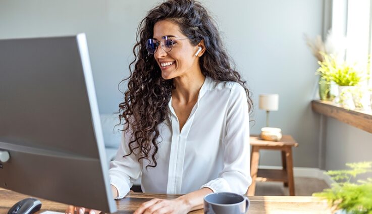 A woman with white shirt and glasses smiling while typing on her computer