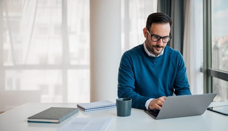 A man with blue sweater looking at his computer
