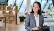 A professionally dressed woman standing with a tablet