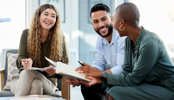 Two women and a man sitting down and speaking with each other in an office setting