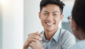 A business casually dressed man smiling at another person