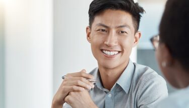 A business casually dressed man smiling at another person