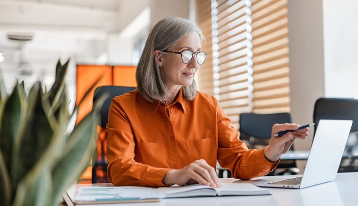 A woman in an orange dress shirt looking at a computer screen