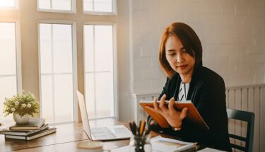 A woman reading a document in a desk next to computer