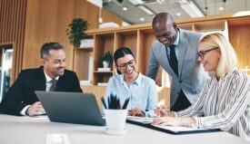 Four professionals laughing in office setting