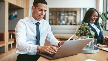 A man wearing business casual clothe is typing on this laptop computer