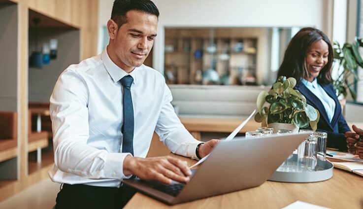 A man wearing business casual clothe is typing on this laptop computer