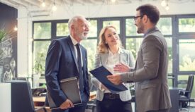 Three professionally dressed people in an office setting speaking with each other
