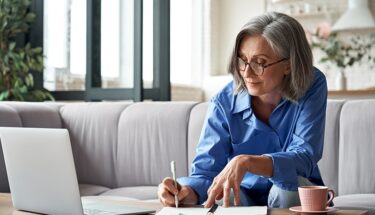 A woman with glasses taking notes on a sheet of paper while sitting on a desk