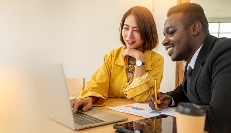 A man and a woman looking at a computer screen in office setting