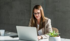 Professionally dressed woman with glasses typing in a computer