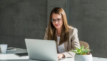 Professionally dressed woman with glasses typing in a computer