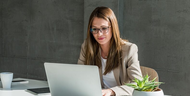 Professionally dressed woman with glasses typing in a computer