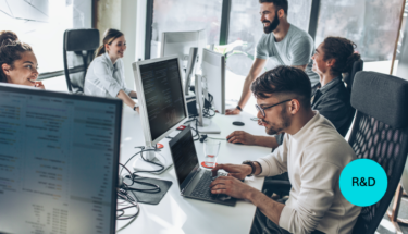 Group of casually dressed men and women work at laptops around a white table.