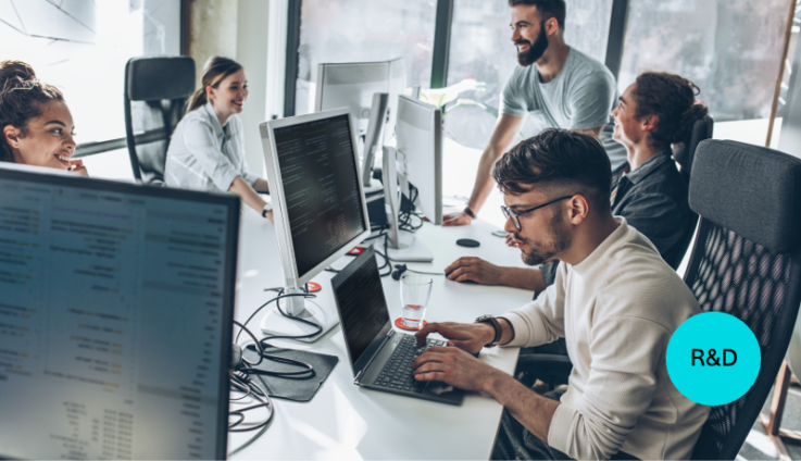 Group of casually dressed men and women work at laptops around a white table.