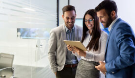 A group of young professionals in business attire smiling and looking at a tablet.